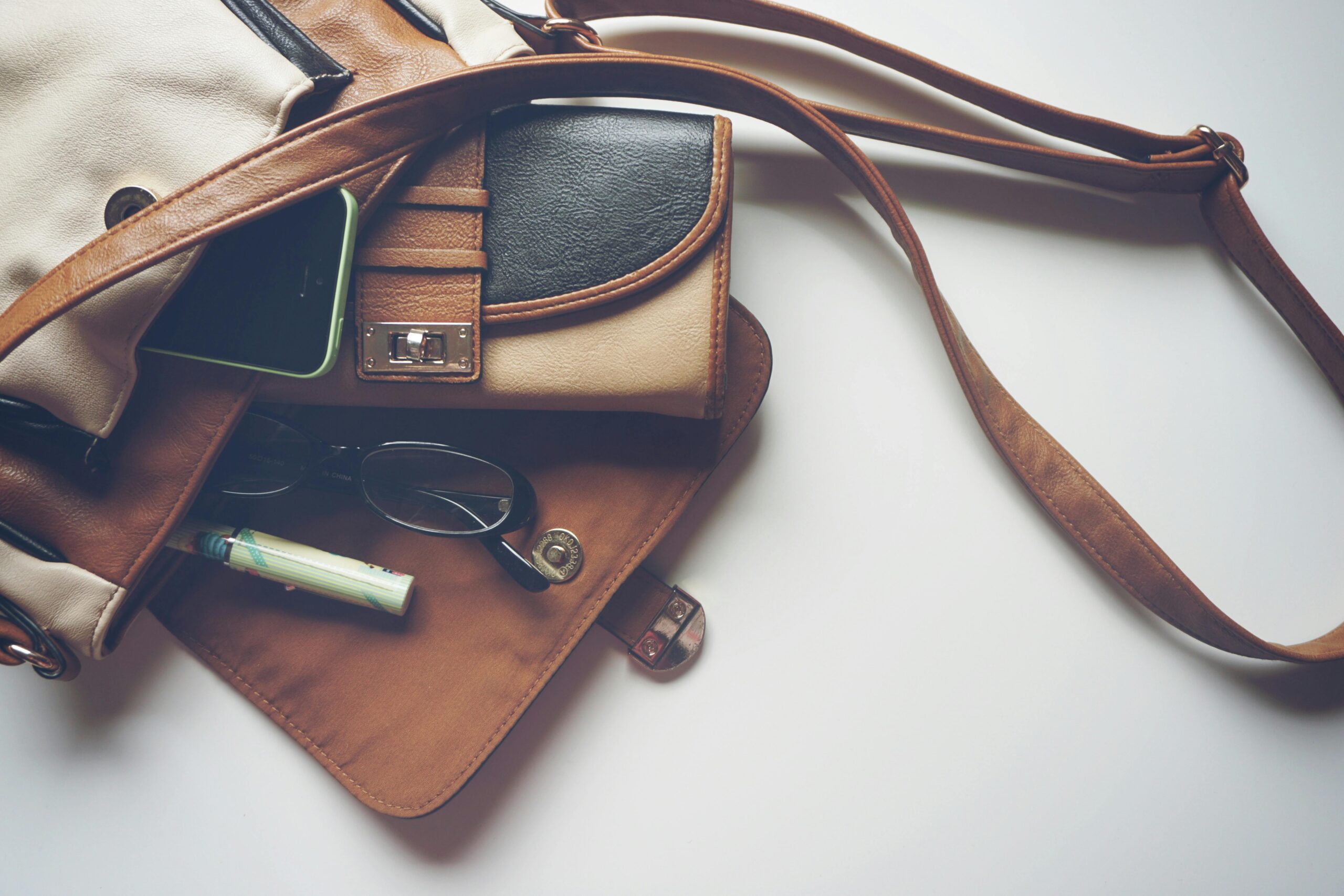 Overhead view of leather bag with eyeglasses, wallet, and smartphone laid out.